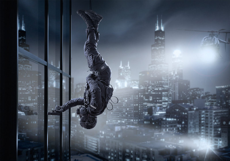 A man of a police special unit ropes upside down from a building at night.